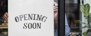 man posting opening soon sign in business storefront window
